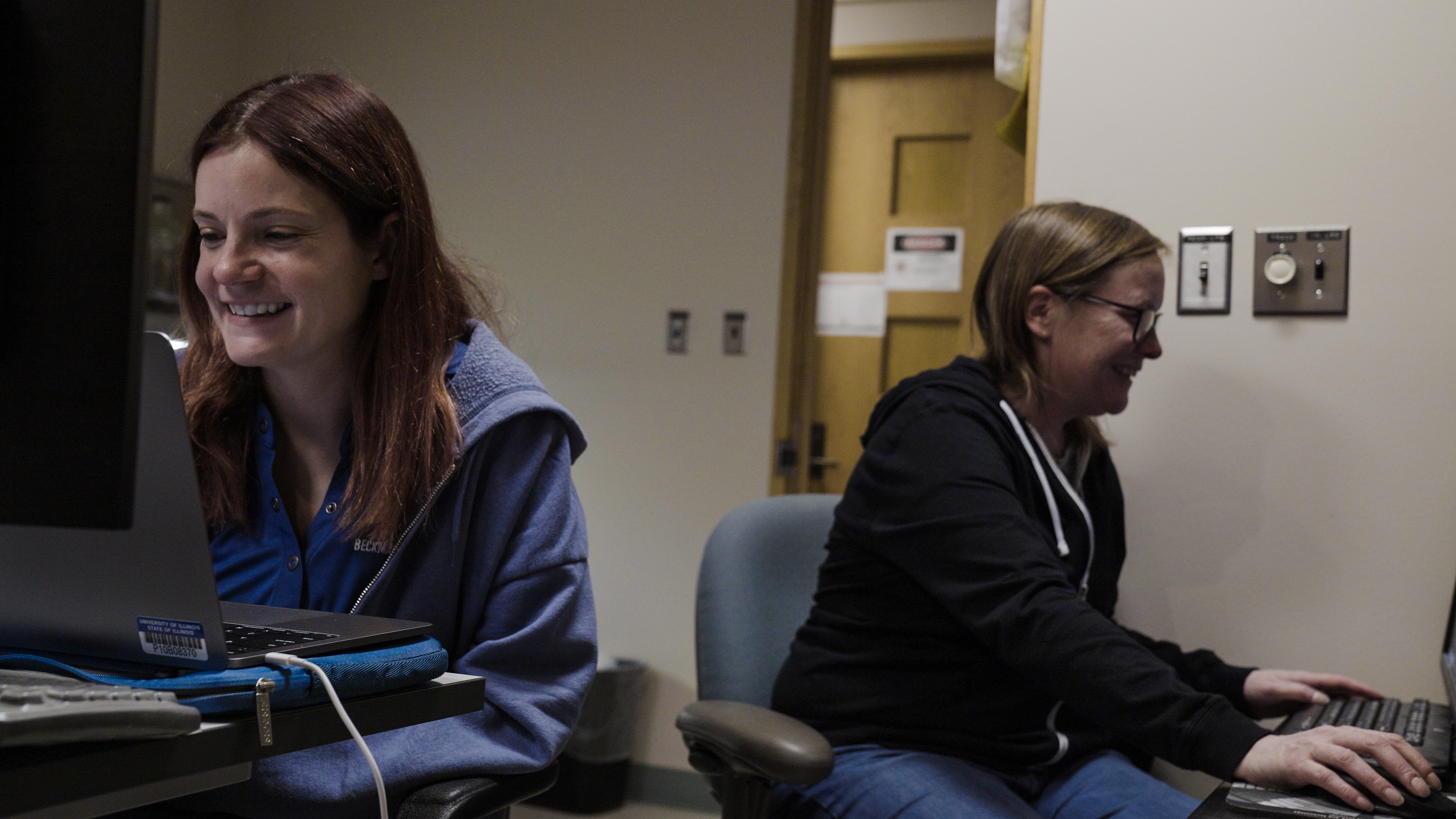 two people smiling while sitting at computers