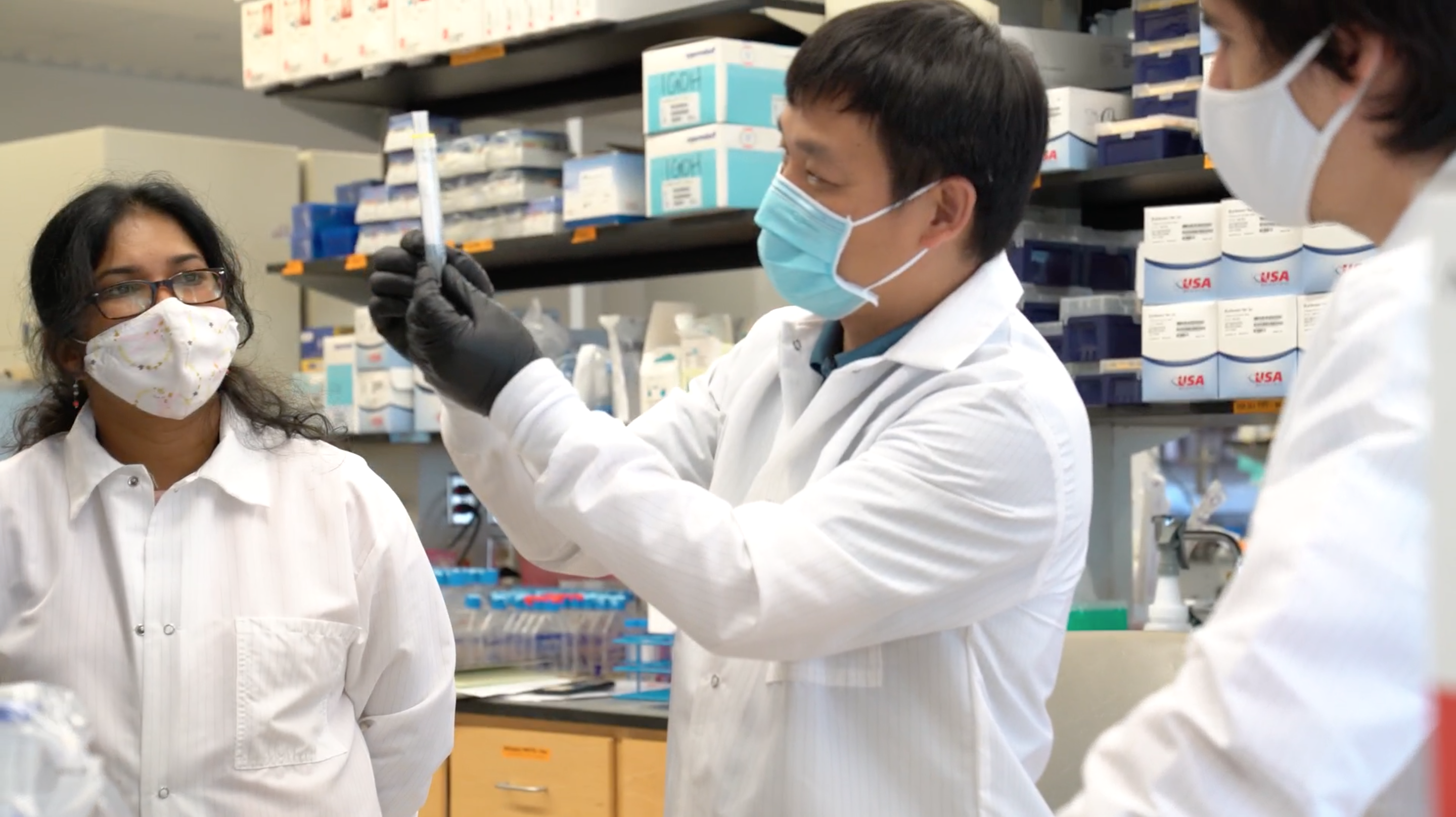 three people, man in middle holding test tube